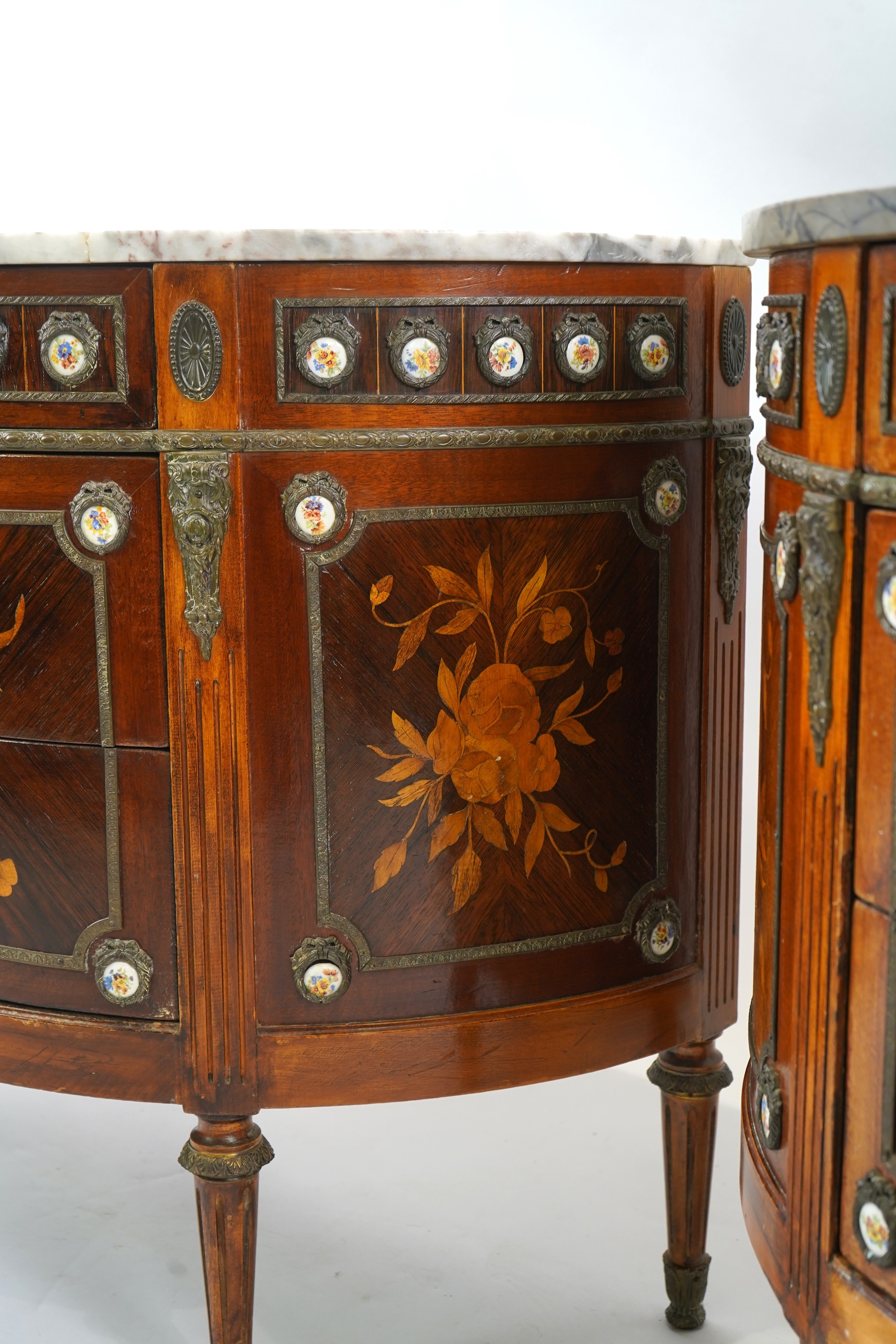 A pair of early 20th century French marquetry inlaid, gilt metal and porcelain mounted rosewood and beech demi-lune commodes